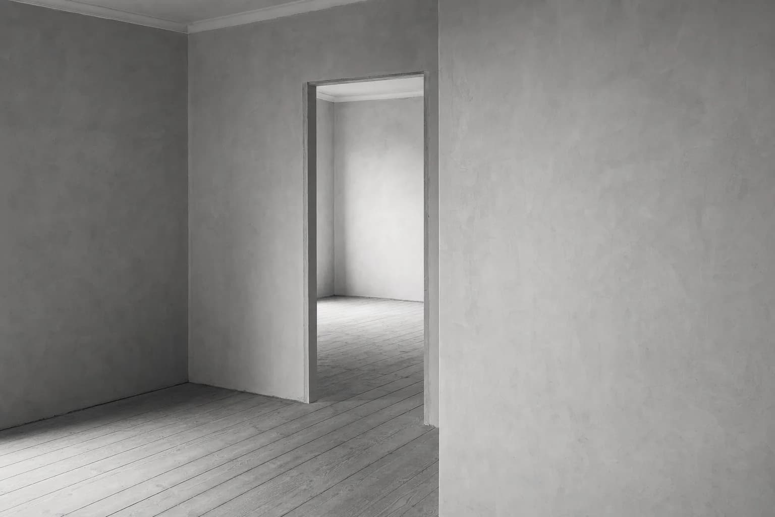 Black and white photograph of an empty domestic room freshly plastered, floorboards sanded back, opening through to a second room