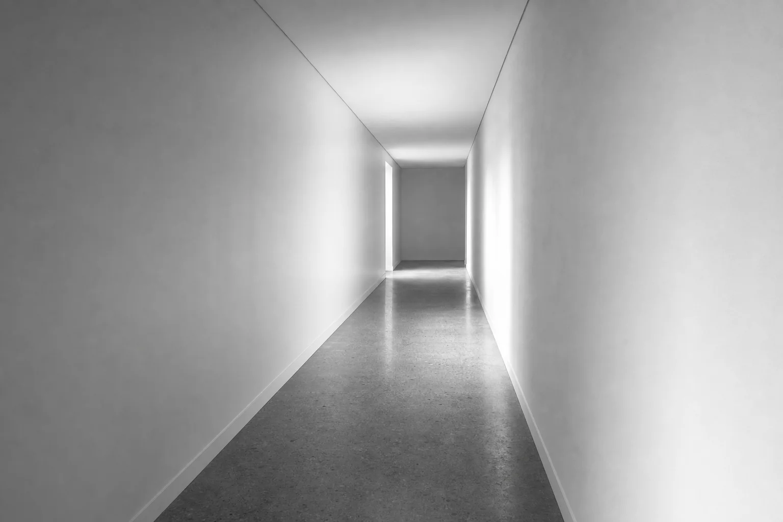Black and white photograph of a long empty corridor inside a completed building running away in perspective