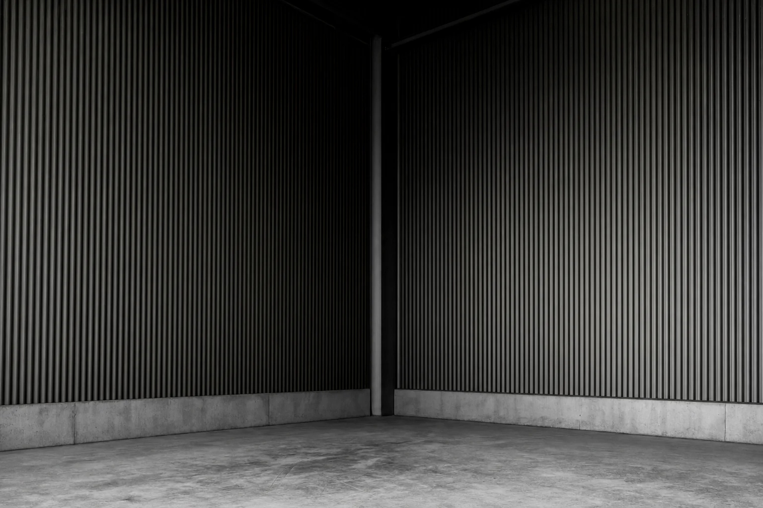 Black and white photograph of the inside corner of a large empty industrial building where two clad walls meet