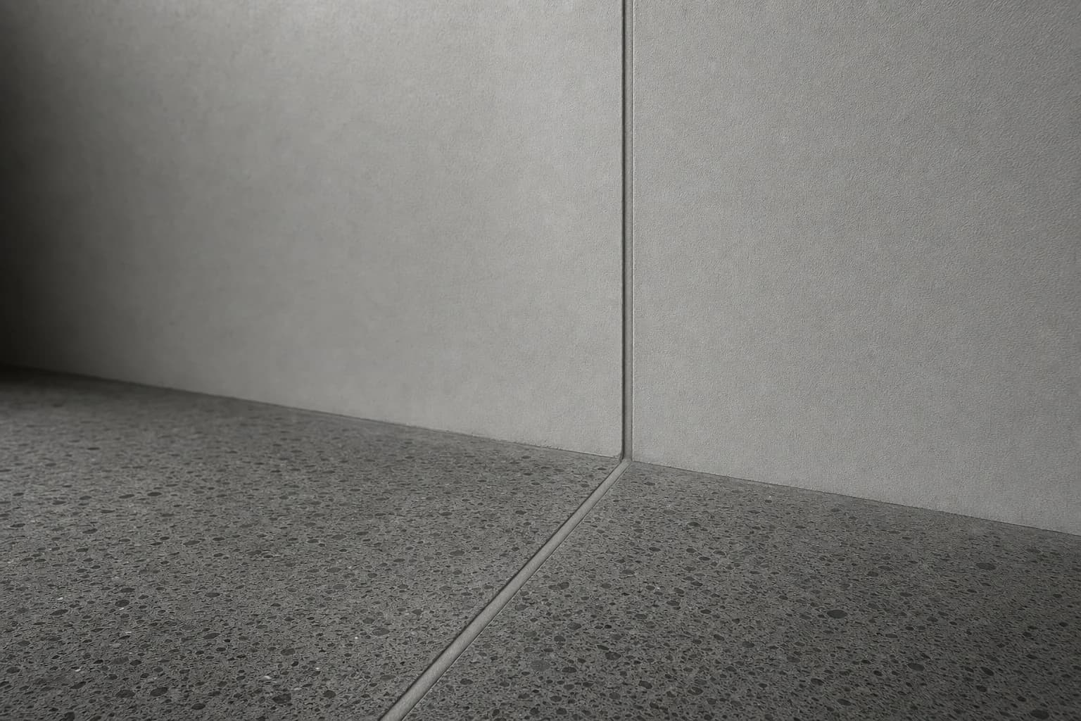 Black and white close detail of a movement joint running across a concrete floor and up a plastered wall, sealed with an even bead