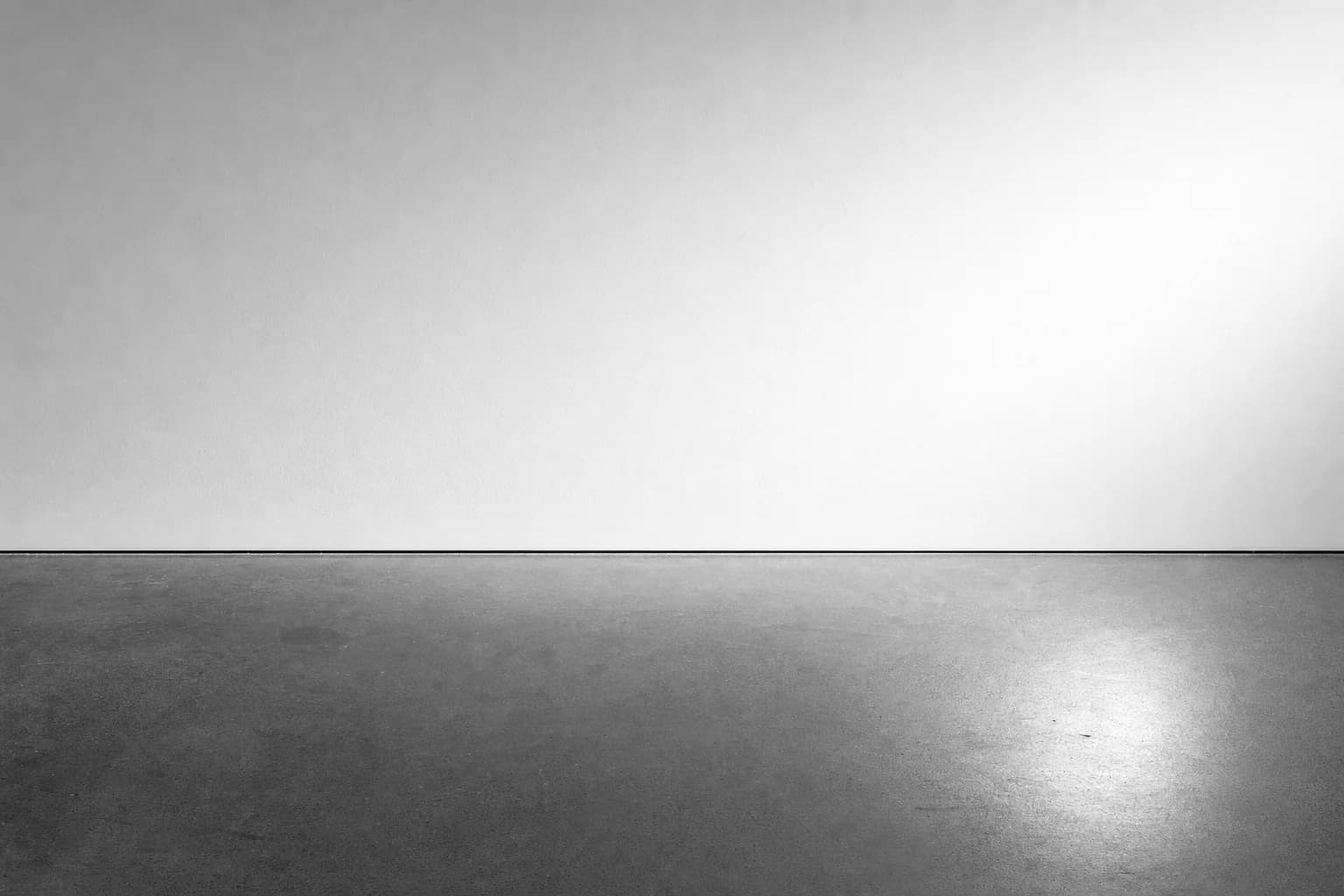 Black and white close detail of a newly plastered wall meeting a sealed floor in one straight line under raking light
