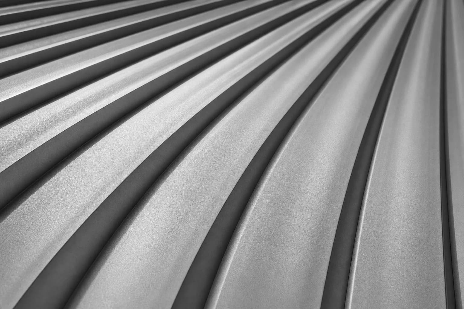 Black and white photograph of profiled metal sheeting seen at an oblique angle, its ribs running away in raking light