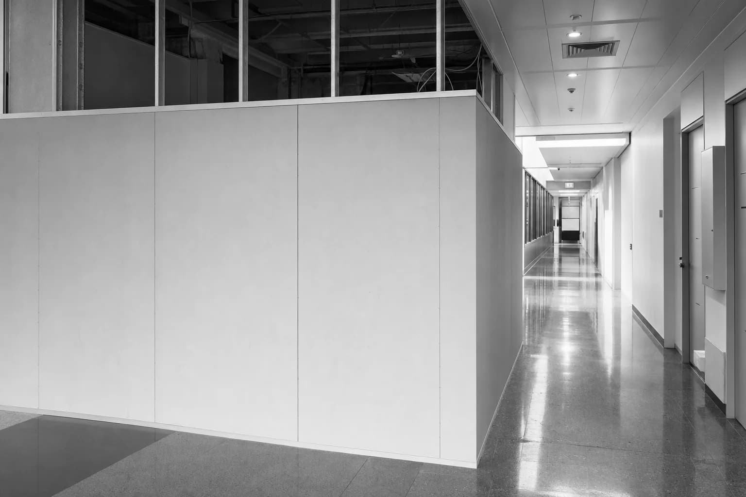 Black and white photograph of temporary works hoarding standing in an occupied institutional corridor