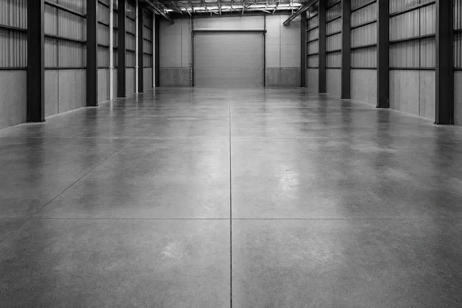 Black and white photograph of a power floated warehouse slab with saw cut control joints running away between steel columns