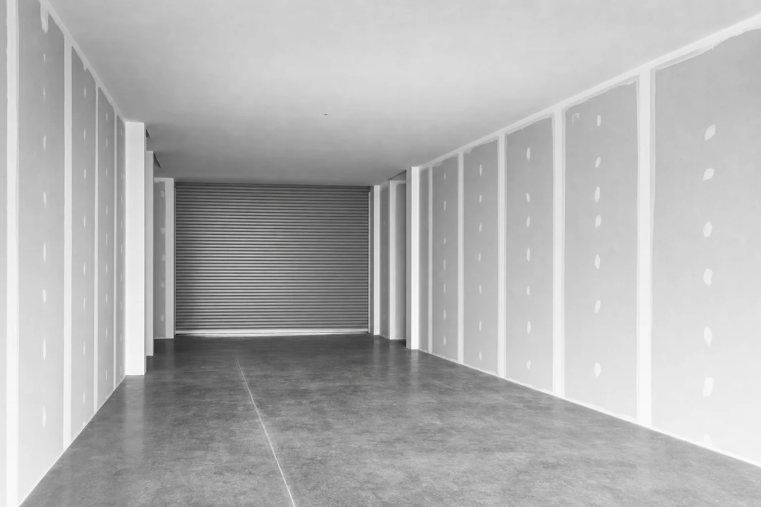 Black and white photograph of an empty retail tenancy shell ready for fitout, roller shutter closed at the rear